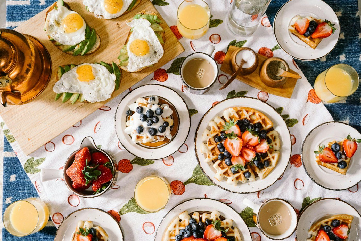 A sunny brunch table with waffles, berries, eggs on avocado toast and fresh orange juice