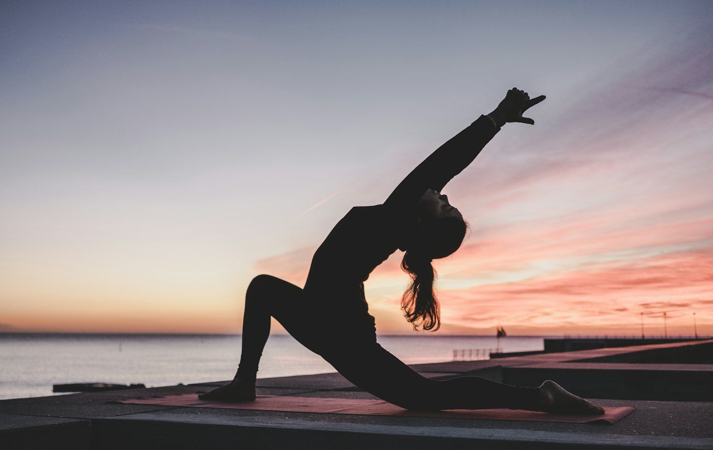 Silhouette of a person in a yoga pose at sunrise by the water