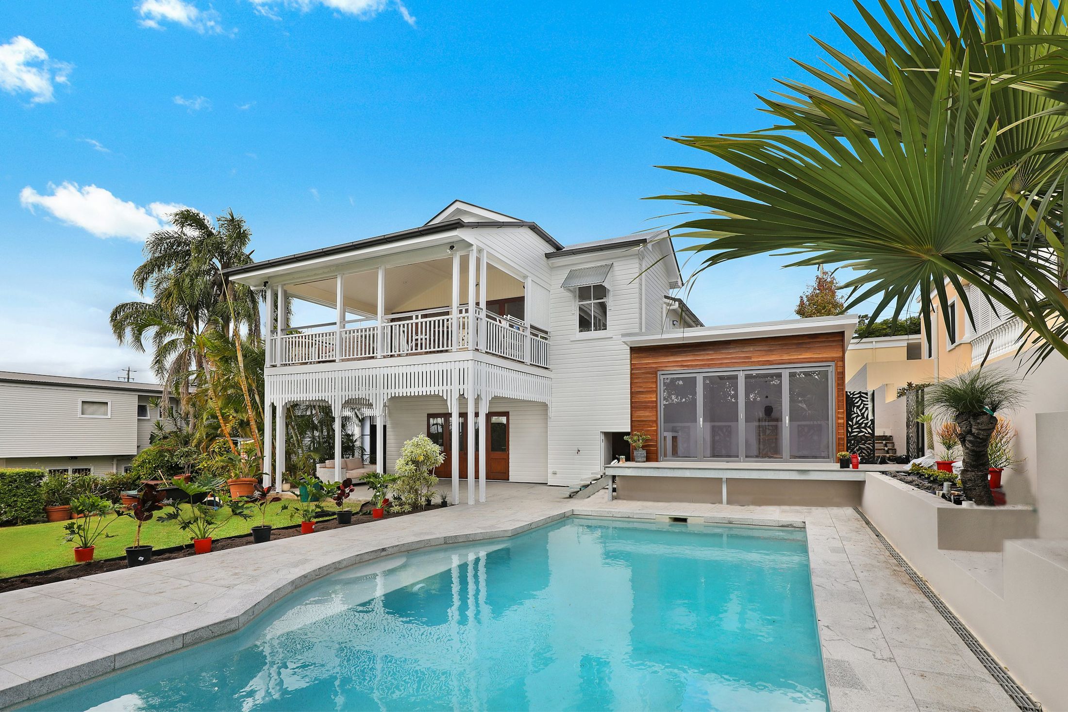 A sparkling blue backyard pool in front of a white two-story Florida home with palm trees